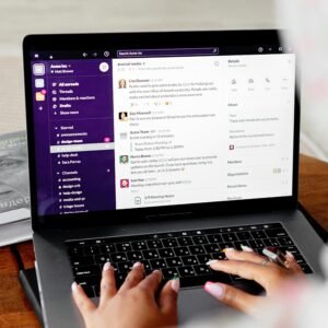 Close-up of hands typing on a laptop displaying Slack for remote communication.